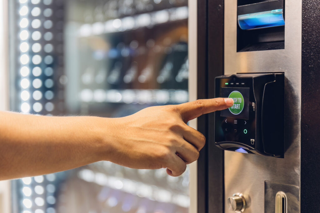 A person’s hand touching a button on a drink machine in El Paso.