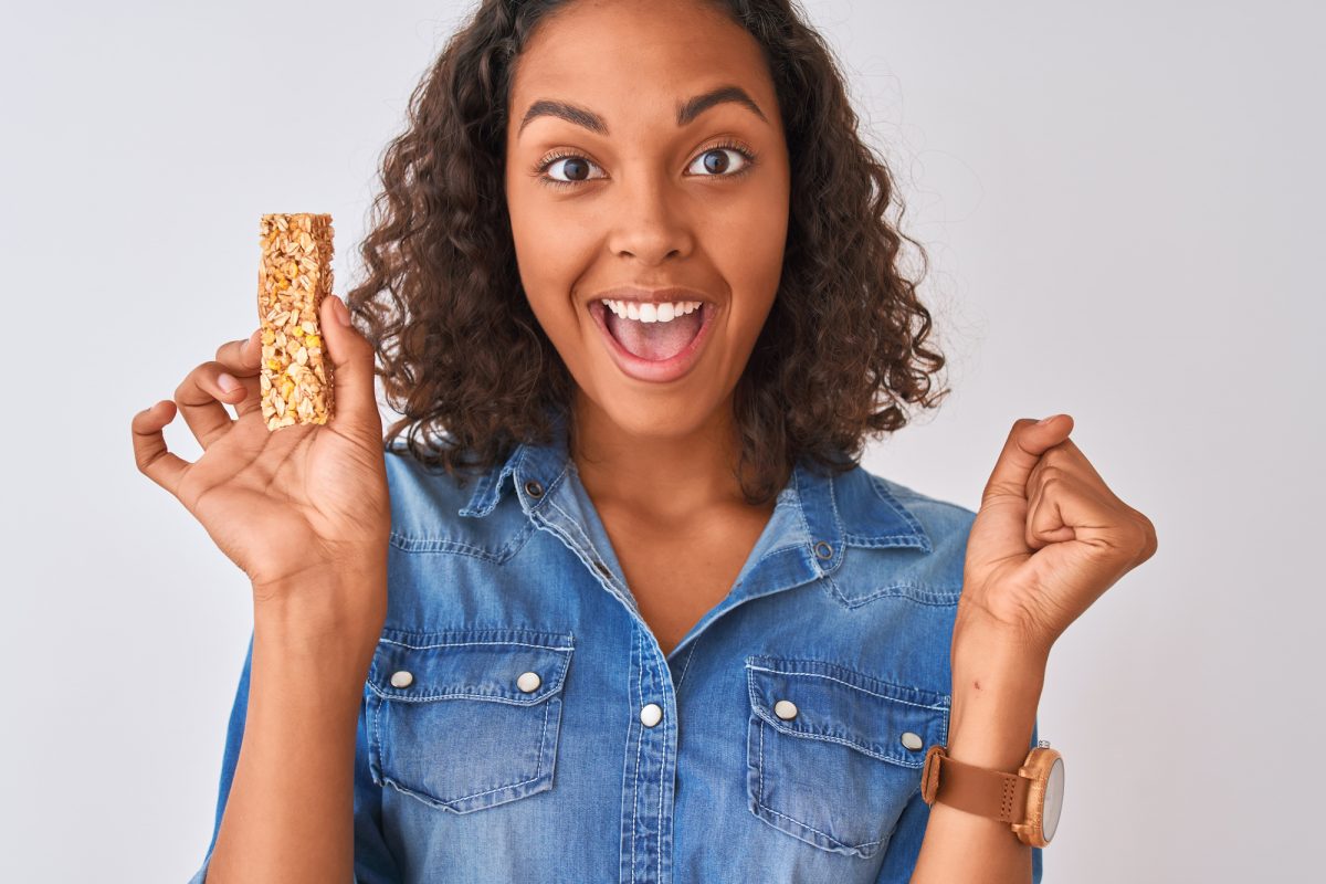 A young woman smiling as she holds a granola bar she bought from a vending machine.
